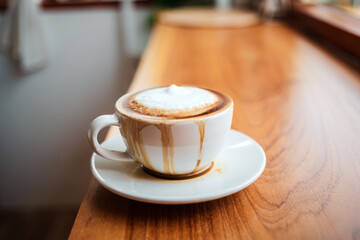 Spilled coffee with milk in a white cup or cappuccino is overflowing from the coffee cup on wooden bar