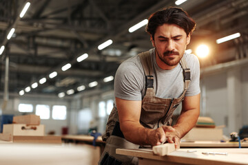 Wall Mural - Young carpenter making wood furniture while working in joinery