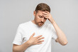 © DimaBerlin - Middle aged man feeling bad puts hand to chest, keeping head having heart pain, headache. Male suffering from heart attack, heartache on grey background. Health problems, high blood pressure, stroke.