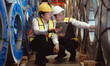 © Nassorn - Skilled manager on job training young technician working in metal sheet production factory. Asian engineer and team sitting in manufacturing facility talking product material protection in warehouse