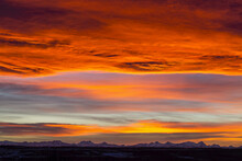 Dramatic Fiery Sunset With Orange And Red Clouds And Mountains In The Distance; Calgary, Alberta, Canada