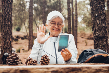 Smiling senior woman in a trekking day in the woods sitting at a wooden table to rest and drink from water bottle. Old people and healthy lifestyle concept