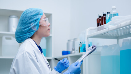 Wall Mural - A female scientist is holding a checklist in front of shelf full of substance glassware. Concept of biology, chemical, microbiology and biotechnology laboratory. Study a Sample of blue substance.