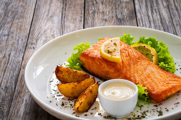 Wall Mural - Seared salmon steak with baked potatoes and fresh vegetable salad served on wooden table
