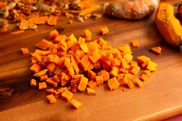 Wall Mural - Diced Fresh Turmeric on a Wooden Cutting Board: Close-up view of peeled and chopped turmeric root with peels in the background