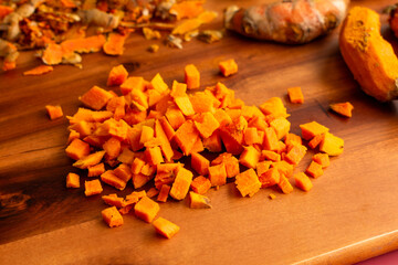 Canvas Print - Diced Fresh Turmeric on a Wooden Cutting Board: Close-up view of peeled and chopped turmeric root with peels in the background