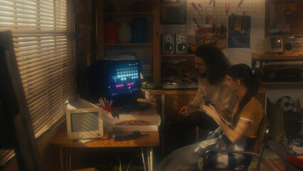 Young male and female co-workers sitting in retro garage office playing console video game during break