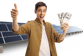 Poster - Happy young man holding stacks of money and gesturing a thumb up sign in front of solar panels