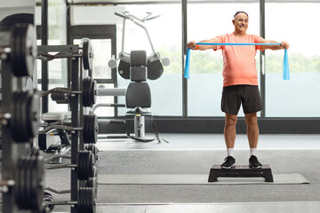 Wall Mural - Mature man in sportswear exercising with a stretch band on a step aerobic platform