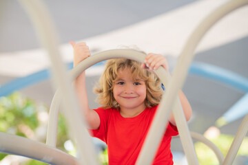 Wall Mural - Outdoor kids portrait on playground. Child climbs up in a park on a playground on a summer day. Childrens playground in a public park. Recreation for children. Kid hanging at outdoor playground.