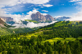 Fototapeta Psy - A vibrant depiction of the Sassolungo Massif and Gardena Valley in Dolomite Alps, Italy. The foreground showcases a lush green valley, while the background highlights a cloud-covered mountain peaks