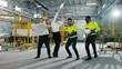 © ihorvsn - Multicultural engineers dancing at modern manufacturing factory and clapping hands. Employees in safety hard hats celebrating succsess at background of welding sparks flying.