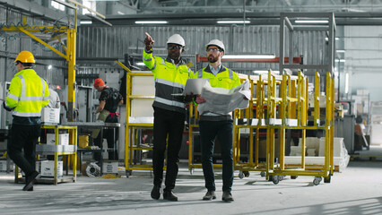 Portrait of male industrial engineers in hard hats discuss new project while using laptop. Two manufactorying employees wearing safety yellow jackets at construction site.