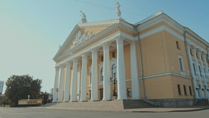 Wall Mural - Establishing shot of 20th century classic style theatre building with yellow walls, white columns, sculptures on roof on sunny morning