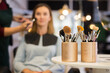 Closeup of set of cosmetic brushes in two organizers on table in beauty salon with makeup artist working with female client on blurred background