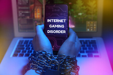 Wall Mural - Internet gaming disorder. Woman with chained hands holding smartphone near laptop on dark background, closeup