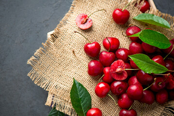 Poster - Sweet red cherry on burlap on a black background. A large number of cherries with leaves on the table, on a black background. close-up.