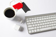 Computer keyboard, cup of coffee, wireless earphones, gift tags with copy space on white background