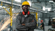 © ihorvsn - African american employee stared, smiling and posing for camera with crossed arms. Male engineer in googles and headphones at manufacture background where welding sparks flying.