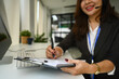 © Prathankarnpap - Smiling female sales consultant in conversation with customer over headset and writing notes on paper