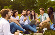 © Studio Romantic - Group of happy, cheerful, diverse, multiethnic student friends sitting on green grass outside, studying information for project together, discussing something, using online tools on modern laptop PC