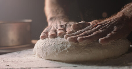 Closeup shot of hands of senior bakery chef applying flour on dough, old man kneading dough, making bread using traditional recipe, isolated on black background Copy space