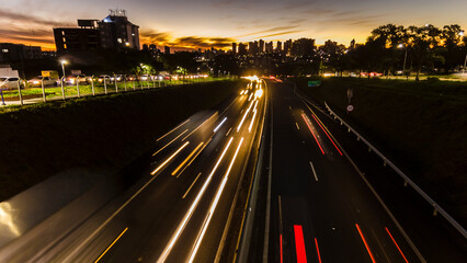 Wall Mural - Trail of light caused by vehicular traffic in Highway with buildings from downtown in the background, in Marília,