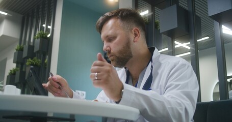 Healthcare specialist sits in medical center cafeteria. Male doctor works on digital tablet computer, examines test results of patient. Canteen worker brings order to medic in clinic or hospital cafe.