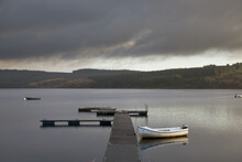 Storm Clouds Brew Over A Tranquil Lake With A Wooden Dock And Boat Moored; Kielder, Northumberland, England