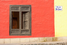 A Window With Ornate Gold Trim And Shutters On A Building Painted Red And Yellow; Lima, Peru