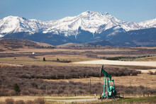 Pumpjack In The Foothills With Snow Covered Mountains And Blue Sky; Longview Alberta Canada