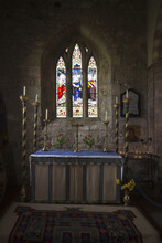 Stained Glass Windows And A Table Surrounded With Candles In A Church; Bamburgh, Northumberland, England