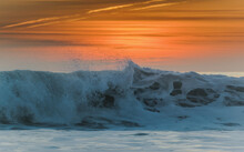 Waves Breaking At The Shore With A Glowing Orange Sky At Sunset; Tarifa, Cadiz, Andalusia, Spain
