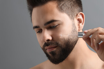 Poster - Handsome man applying cosmetic serum onto face on grey background, closeup