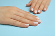 © New Africa - Woman showing her manicured hands with white nail polish on light blue background, closeup