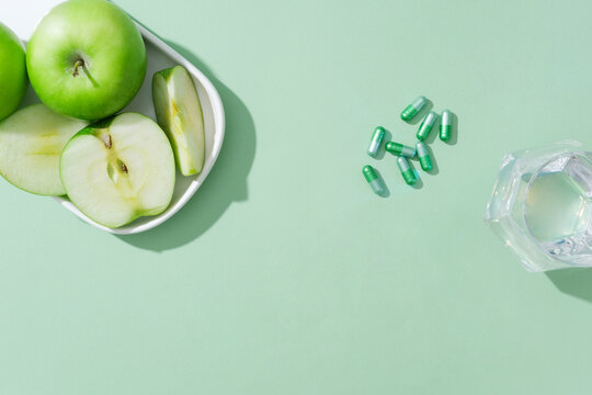 against the green background, dishes of green apples with capsule pills and glass cup decorated. bla