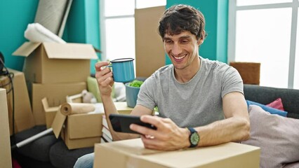 Sticker - Young hispanic man watching video on smartphone drinking coffee at new home