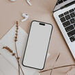 Cell phone with blank screen, laptop, earphones, dried grass on tan beige table. Styled flat lay mock up with empty copy space. Designed top view mobile phone mockup