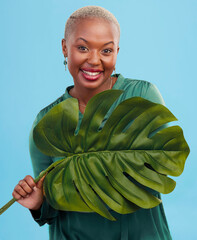 Poster - Black woman, monstera leaf and beauty, face with natural cosmetics and fashion on blue background. Silk green dress, eco friendly skincare and dermatology, African model glow and portrait in studio