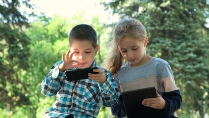 Wall Mural - Children use gadgets while sitting in the park outdoors, games on smartphone and tablet