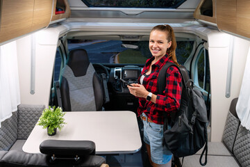 Happy young woman standing in camper van and smiling while choosing motorhome to rent.