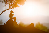 Fototapeta  - A tourist man sitting on the rock and take photo sunset orange color background