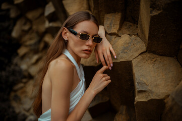 Wall Mural - Fashionable confident woman wearing trendy black rectangular sunglasses, posing on rocks. Outdoor close up fashion portrait. Copy, empty space for text