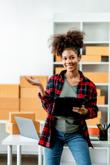 Young African woman prepares parcel boxes and checks online orders for delivery to customers on laptop. Shipping and online shopping concepts