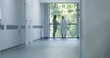 © Framestock - Hospital hallway: Doctors and professional medics walk. Nurse with digital tablet comes to elderly female patient standing near window. Medical staff and patients in clinic or medical center corridor.