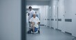 © Framestock - Male doctor stands with elderly woman in wheelchair in clinic corridor, uses mobile phone. Medic with female patient near operating or procedures room. Medical staff and patients in hospital hallway.