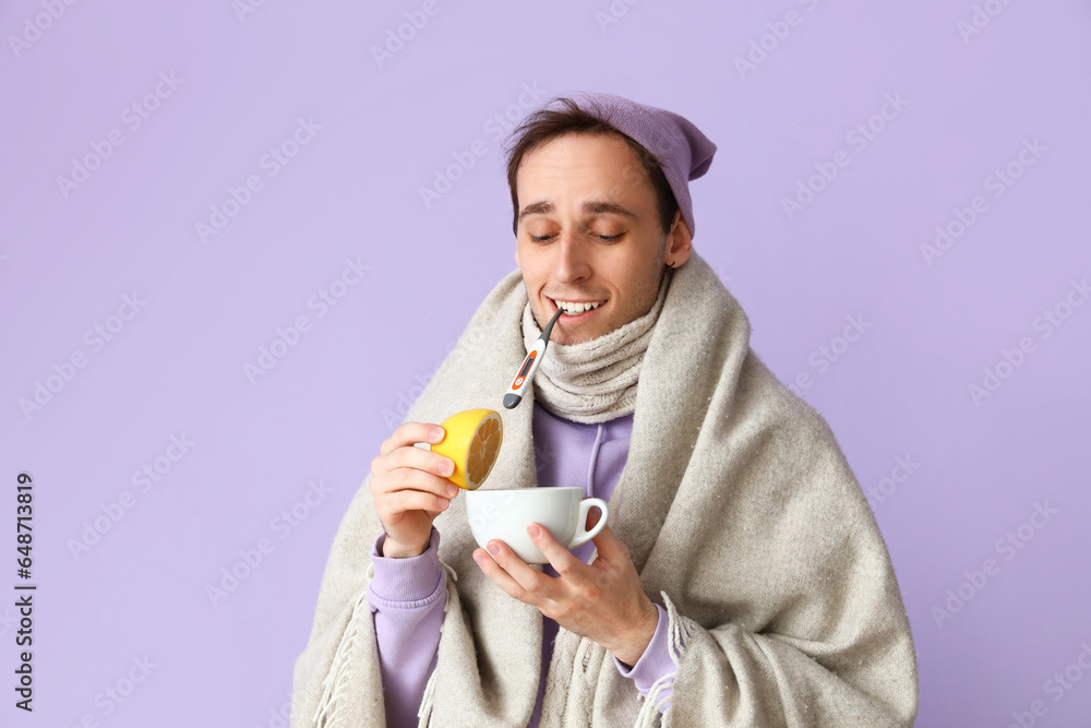 Ill young man with lemon and cup of tea on lilac background