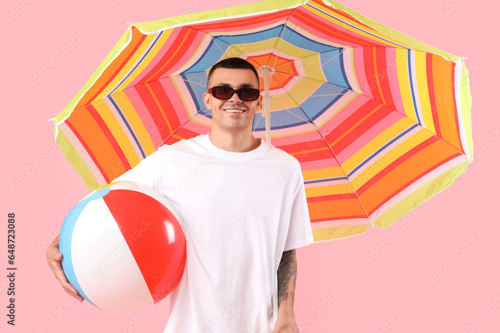 Happy young man with inflatable ball and umbrella on pink background