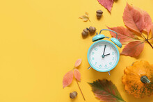 Alarm Clock With Autumn Leaves And Pumpkin On Orange Background