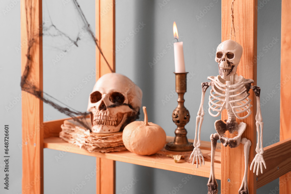 Candle with Halloween decor on shelf near dark wall, closeup